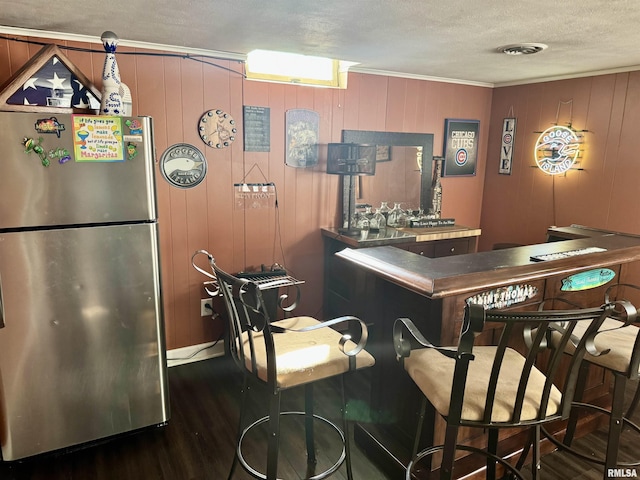 bar featuring dark wood finished floors, freestanding refrigerator, ornamental molding, a textured ceiling, and a dry bar