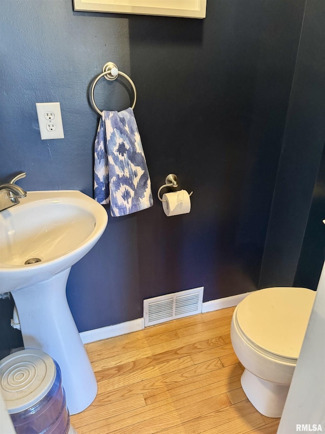 half bath with visible vents, baseboards, toilet, wood finished floors, and a sink