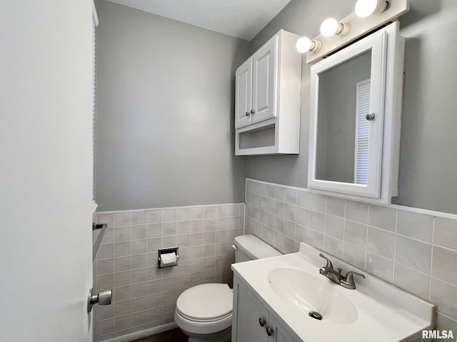 bathroom with a wainscoted wall, toilet, tile walls, and vanity