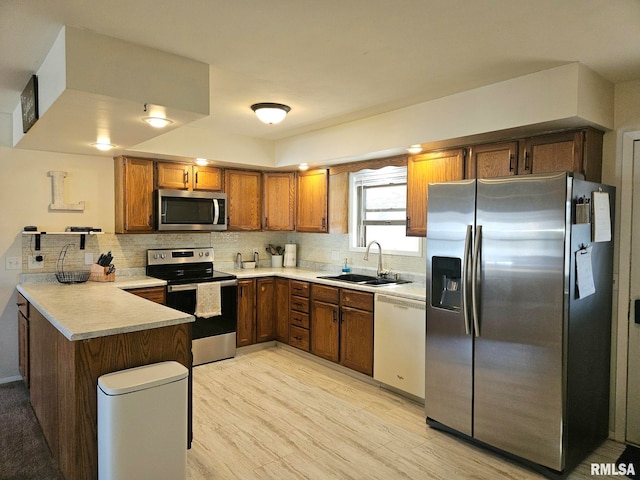 kitchen featuring brown cabinetry, a peninsula, a sink, decorative backsplash, and stainless steel appliances