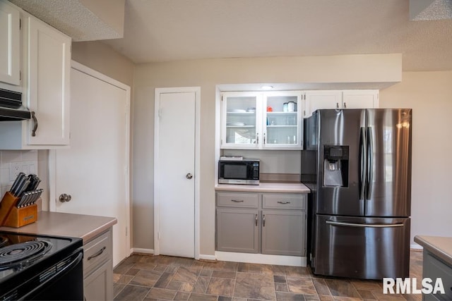 kitchen featuring stone finish flooring, glass insert cabinets, under cabinet range hood, appliances with stainless steel finishes, and white cabinetry