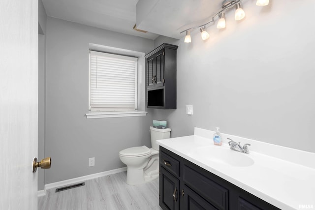 bathroom with visible vents, toilet, wood finished floors, baseboards, and vanity