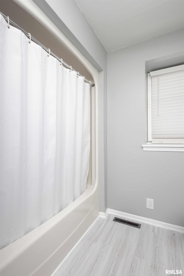 bathroom featuring visible vents, shower / bath combo, baseboards, and wood finished floors