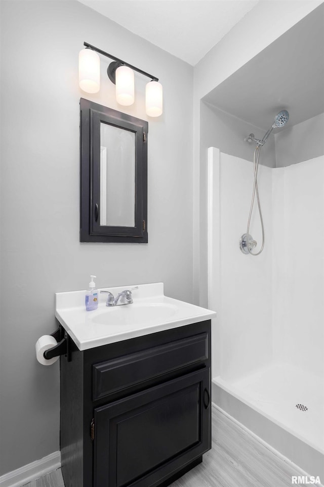 full bathroom with baseboards, vanity, walk in shower, and wood finished floors