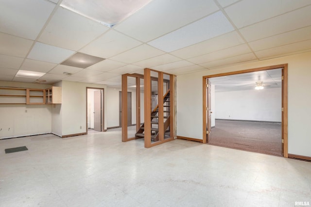 finished basement featuring tile patterned floors, stairway, baseboards, and a drop ceiling