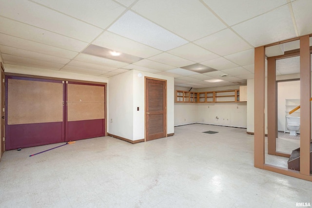 finished basement with tile patterned floors, a drop ceiling, stairs, and baseboards