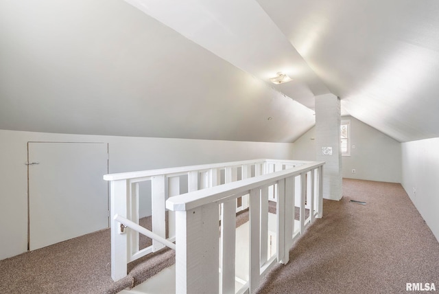 hallway with an upstairs landing, carpet floors, and vaulted ceiling