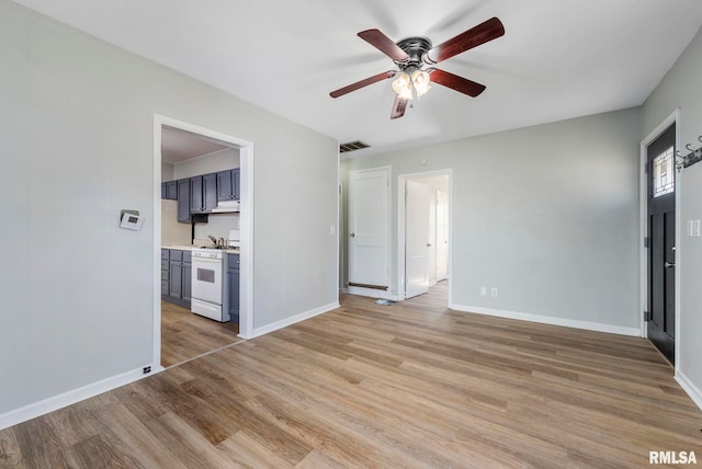 unfurnished living room featuring light wood-style flooring, a ceiling fan, visible vents, and baseboards