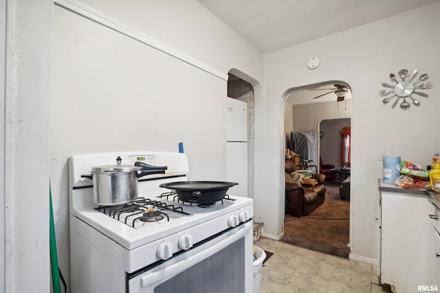 kitchen featuring white appliances, white cabinets, baseboards, and arched walkways