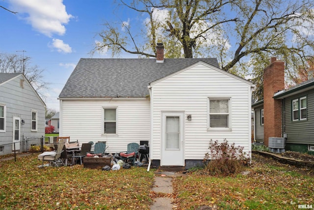 back of property with central air condition unit, roof with shingles, a chimney, and fence