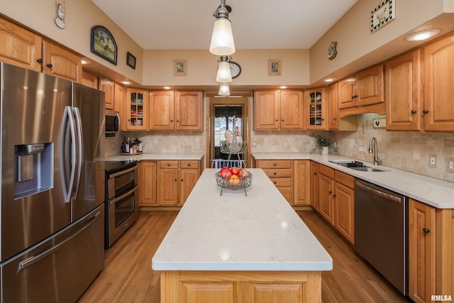 kitchen featuring a sink, a center island, stainless steel appliances, light wood finished floors, and decorative backsplash