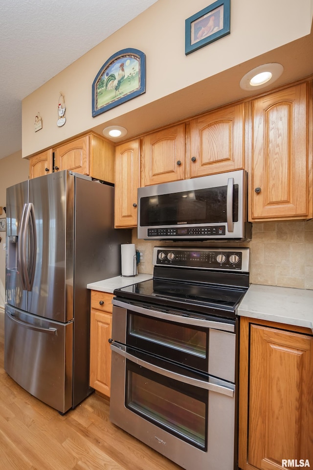 kitchen with stainless steel appliances, light wood finished floors, backsplash, and light countertops