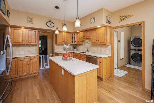 kitchen with a kitchen island, light countertops, stacked washing maching and dryer, stainless steel appliances, and a sink