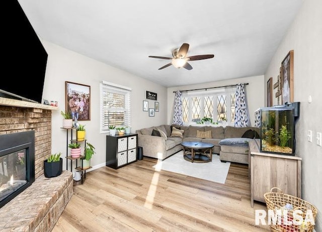 living room featuring wood finished floors, a brick fireplace, a ceiling fan, and a healthy amount of sunlight