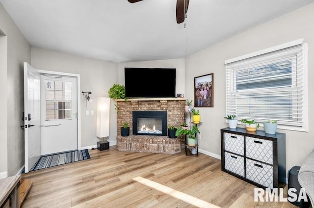 living room with a wealth of natural light, a brick fireplace, a ceiling fan, and wood finished floors