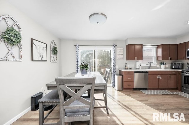 kitchen with light wood-type flooring, a sink, stainless steel appliances, light countertops, and baseboards