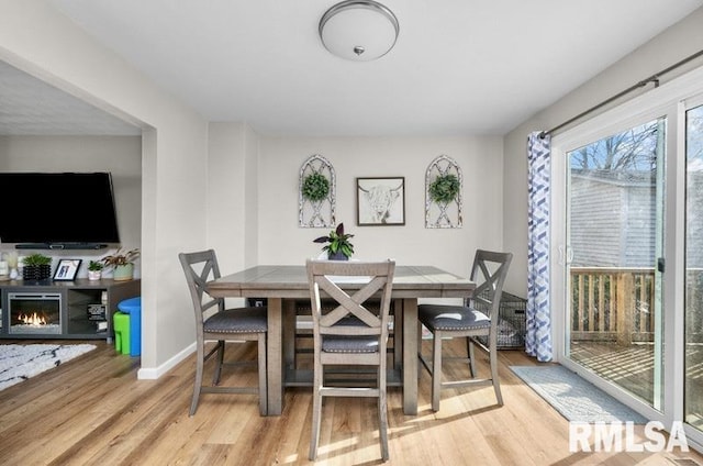 dining area with a glass covered fireplace, baseboards, and wood finished floors