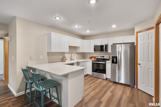 kitchen featuring a peninsula, a breakfast bar area, light wood-style floors, and appliances with stainless steel finishes