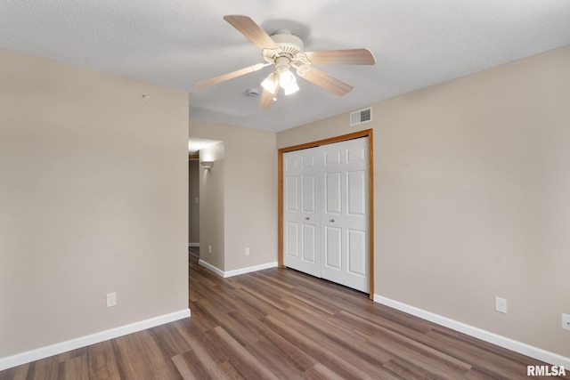 unfurnished bedroom featuring a ceiling fan, wood finished floors, baseboards, visible vents, and a closet