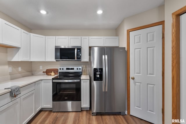 kitchen with stainless steel appliances, wood finished floors, white cabinets, and light countertops