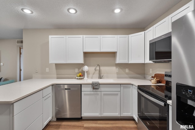 kitchen with a sink, white cabinetry, appliances with stainless steel finishes, a peninsula, and light countertops