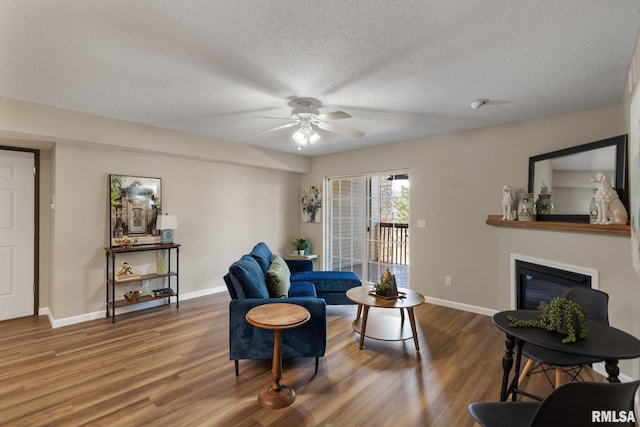 living room featuring a glass covered fireplace, baseboards, wood finished floors, and a ceiling fan