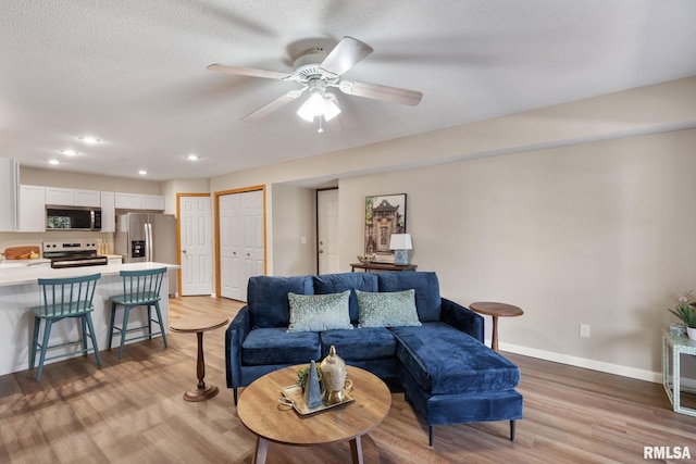 living room with a ceiling fan, baseboards, light wood finished floors, recessed lighting, and a textured ceiling