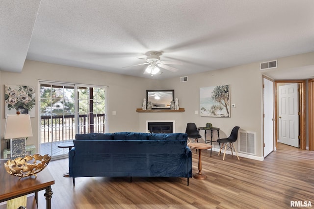 living area with a glass covered fireplace, wood finished floors, visible vents, and ceiling fan