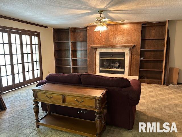 carpeted living area with a ceiling fan, a tile fireplace, and a textured ceiling