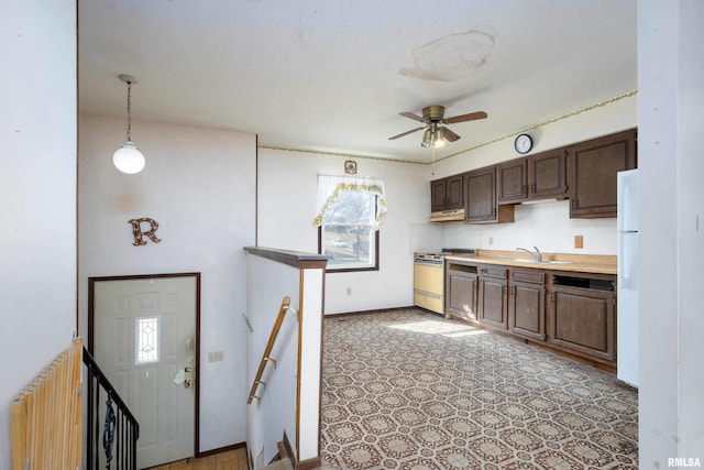 kitchen featuring ceiling fan, dark brown cabinetry, light countertops, gas stove, and a sink