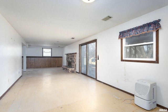 empty room with light floors, baseboards, visible vents, wainscoting, and a brick fireplace