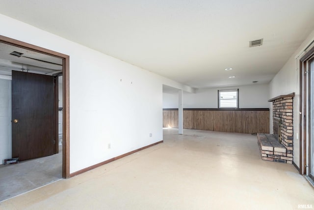 spare room featuring wooden walls, wainscoting, a fireplace, and light floors