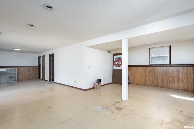 basement with light floors, wood walls, and wainscoting