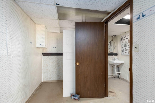 hall with a drop ceiling, wallpapered walls, and unfinished concrete flooring