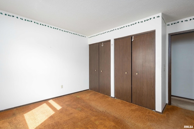 unfurnished bedroom featuring baseboards, a textured ceiling, multiple closets, and carpet floors