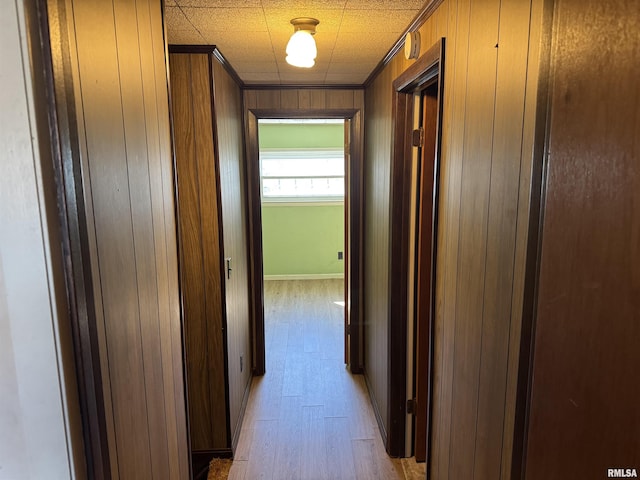 hallway featuring crown molding, wooden walls, and light wood-style floors