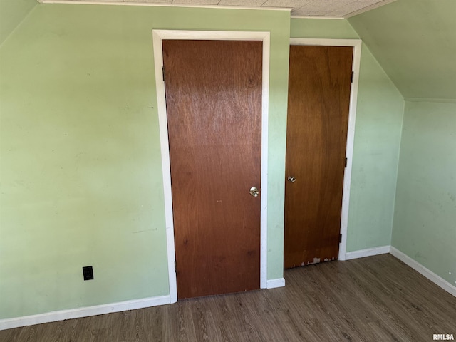 unfurnished bedroom featuring a closet, lofted ceiling, baseboards, and wood finished floors