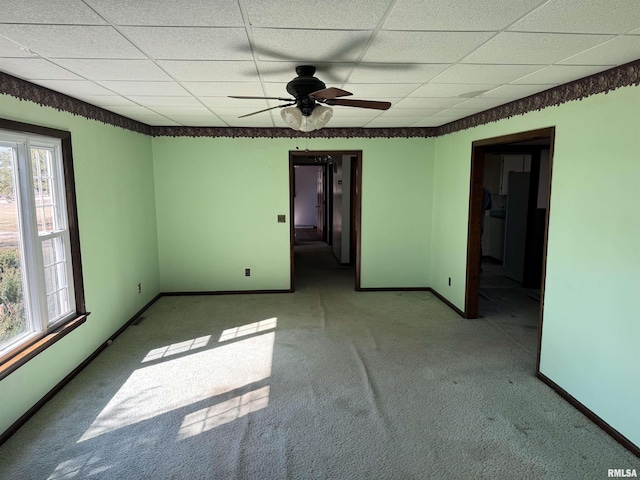 carpeted spare room with a drop ceiling, baseboards, and ceiling fan