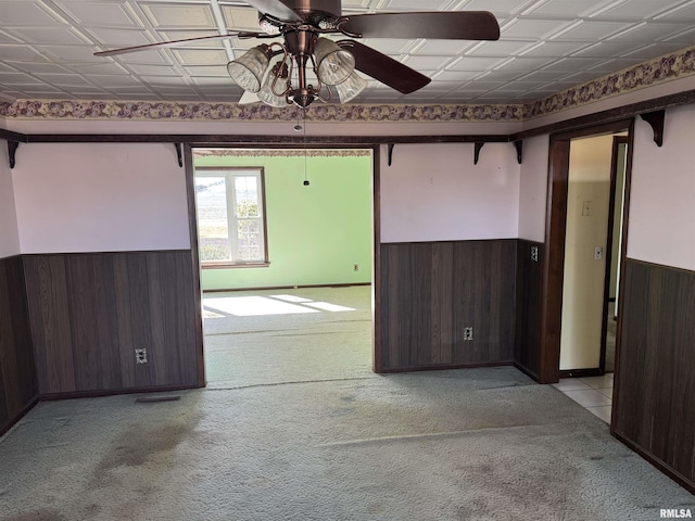 spare room with wooden walls, ceiling fan, carpet floors, wainscoting, and an ornate ceiling