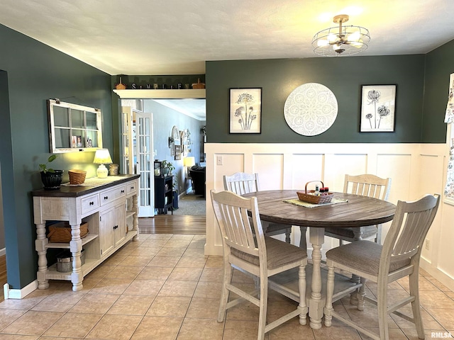 dining area with light tile patterned floors, a decorative wall, french doors, and a wainscoted wall