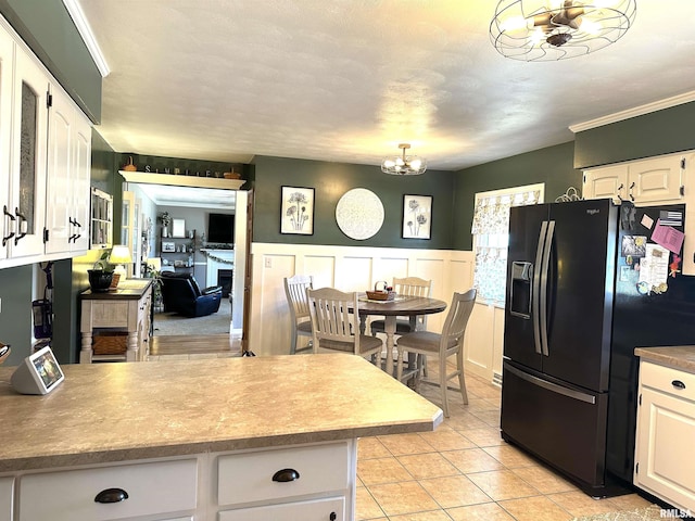 kitchen featuring a wainscoted wall, an inviting chandelier, a peninsula, white cabinets, and black fridge