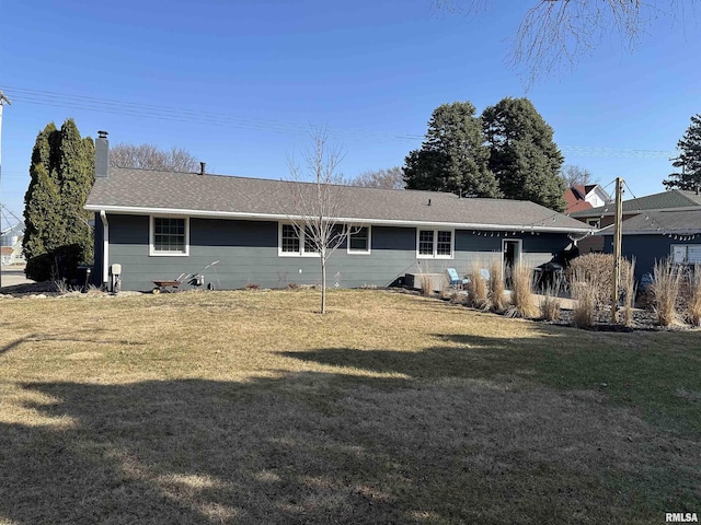 rear view of house featuring a lawn, roof with shingles, and a chimney