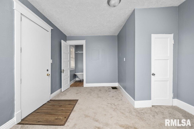 interior space featuring ensuite bath, baseboards, carpet floors, and a textured ceiling