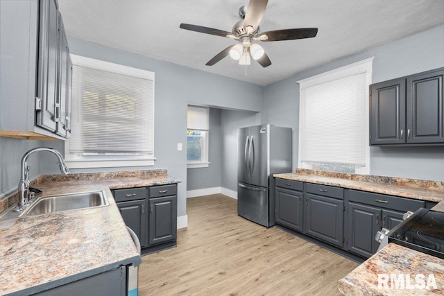 kitchen with baseboards, light wood-style flooring, freestanding refrigerator, ceiling fan, and a sink