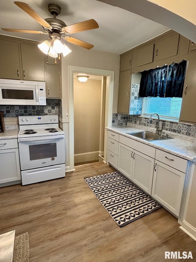 kitchen featuring light countertops, light wood-type flooring, decorative backsplash, white appliances, and a sink