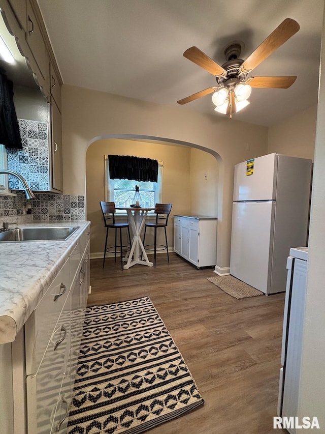 kitchen with wood finished floors, arched walkways, freestanding refrigerator, a sink, and range