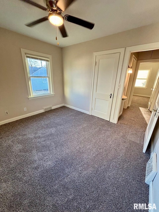 unfurnished bedroom featuring baseboards, visible vents, dark carpet, and ceiling fan