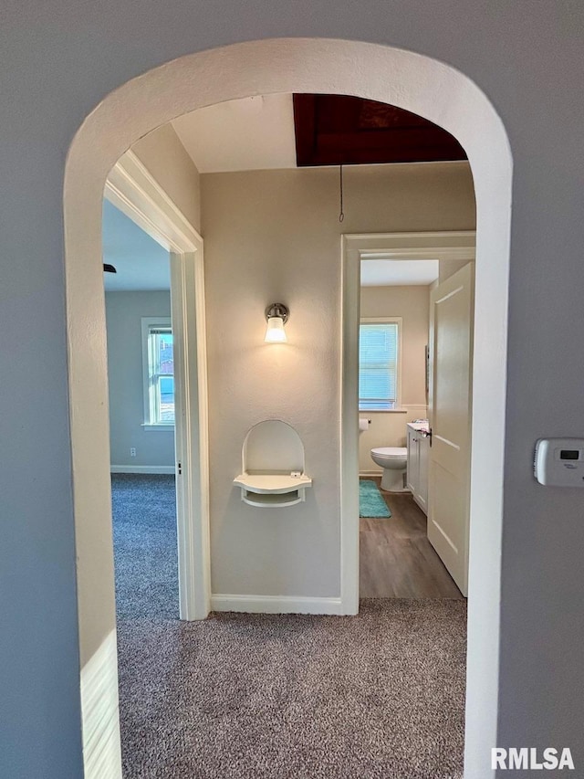 corridor featuring arched walkways, baseboards, and carpet floors