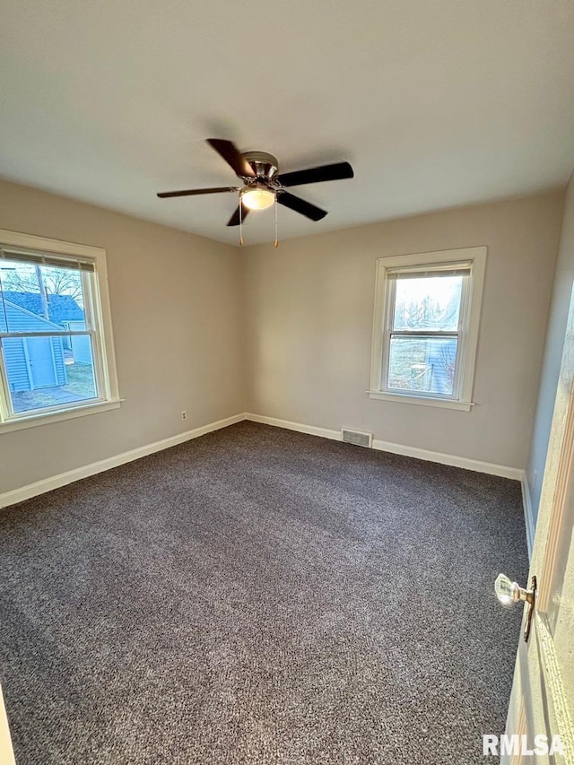 unfurnished room with baseboards, visible vents, dark carpet, and ceiling fan