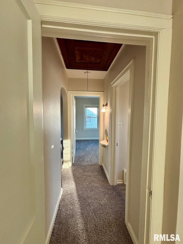 hallway featuring attic access, baseboards, a tray ceiling, and carpet floors